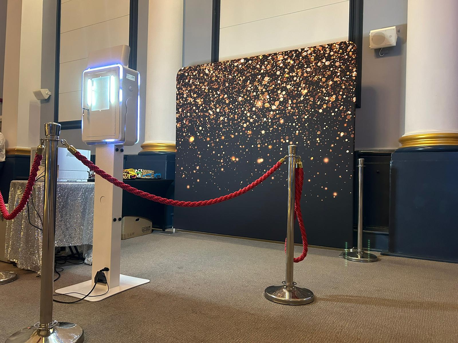 Photo booth with gold sparkle backdrop and red rope barriers